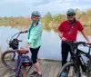 Two people possibly a couple are standing with their bicycles on a lakeside wooden deck smiling for a photo in a serene outdoor setting