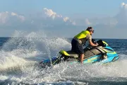 A person is actively maneuvering a jet ski over the ocean waves, creating a dynamic splash of water.