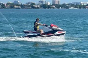 A person is riding a jet ski on a clear day with a cityscape in the background.