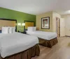The image shows a neatly arranged hotel room with two beds a desk a framed picture on the wall and a green accent wall