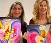 Two people are holding vibrant abstract paintings with heart shapes as the central theme