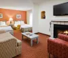 The image shows a well-furnished hotel room with twin beds a seating area a fireplace and a wall-mounted flat-screen TV