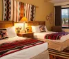 The image shows a warmly decorated bedroom with a large bed adorned with a colorful geometric-patterned blanket complementing the Southwestern-style rug on the floor and with a scenic view through a window