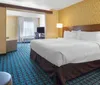 The image depicts a neatly arranged hotel room with a large bed a desk area a flat-screen TV and patterned carpeting