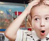 A surprised young child is wide-eyed and holding their head with their mouth open in front of a backdrop featuring the Guinness World Records logo