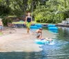 A family enjoys a sunny day at a lazy river with children playing in the water and an adult supervising