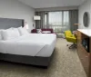 This image shows a modern and neatly organized hotel room with a large bed a sitting area with a couch and armchair a work desk and a television set over a cabinet