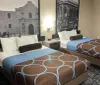 The image shows a hotel room with two beds each adorned with a brown and blue patterned bedspread flanked by large black and white photographs on the wall
