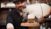 A bartender pours a smoke-infused drink, creating a dramatic visual effect.