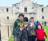 A group of four people are posing for a photo in front of the Alamo on a cloudy day