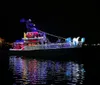 A person on a boat watches a vibrant blue firework display over the water at night with a Frisky Mermaid Dolphin Tours  Boat Rentals logo in the upper left