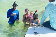 A group of people appears to be engaged in a snorkeling activity, with some participants in the water and others on a boat, and one individual holding a net with marine life to show the others.