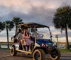 A family enjoys a scenic ride in a golf cart against a backdrop of palm trees and a sunset sky