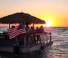 A group of people enjoy a sunset from a thatched-roof boat adorned with an American flag on the open sea