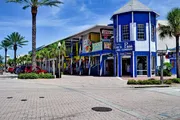 The image shows a vibrant street scene with colorful storefronts, palm trees, and a clear blue sky.