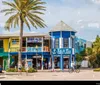 The image shows a vibrant street scene with colorful storefronts palm trees and a clear blue sky