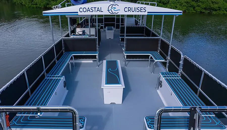 The image shows an empty double-decker party boat from an aerial perspective, featuring neat rows of benches, a steering station, and the name COASTAL CRUISES printed on its canopy.