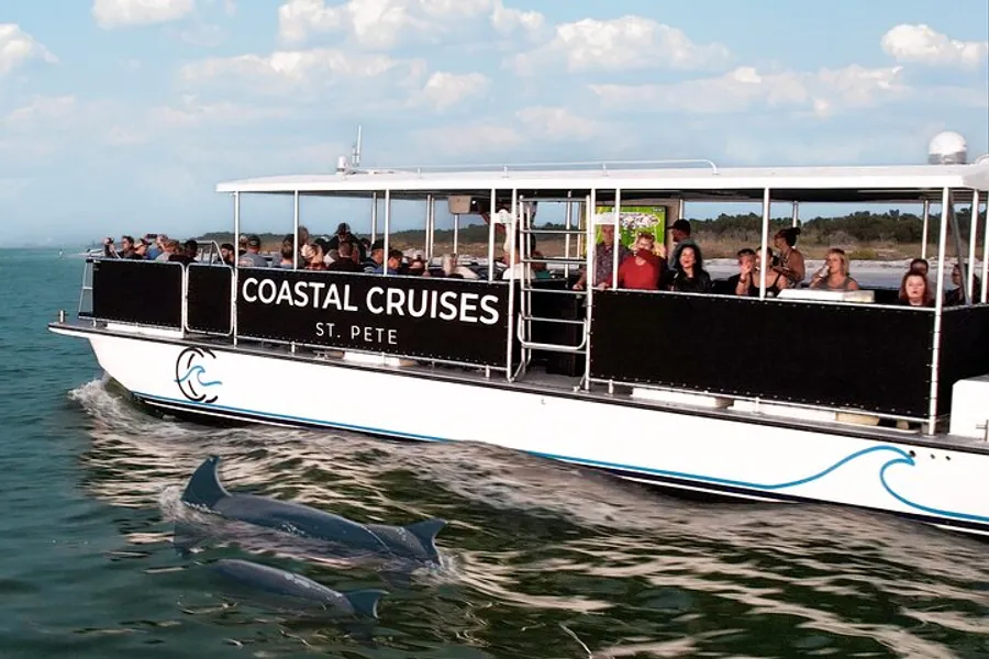 A Coastal Cruises boat with passengers appears to be enjoying a sightseeing tour as dolphins swim nearby.