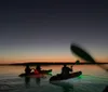 A person is kayaking at night on calm water illuminated by a bright green underwater light
