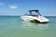 A white and green speedboat is floating on clear blue waters under a sunny sky.