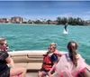 A group of people including two children wearing life jackets are on a boat excitedly watching a dolphin leap out of the water in a sunny coastal setting