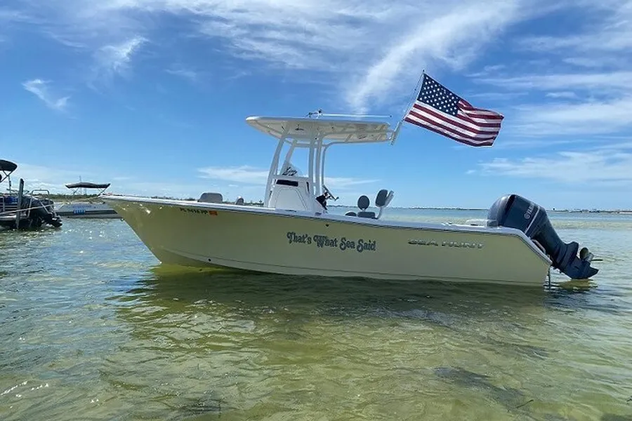 A boat named That's What Sea Said is anchored in shallow water with the American flag flying from the rear under a clear blue sky.