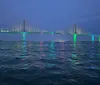 A large illuminated suspension bridge spans across the water at twilight its lights reflected on the waters surface