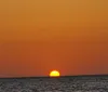 The image captures a tranquil sunset with the sun half-dipped below the horizon over a calm sea emitting a warm orange glow that fills the sky