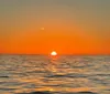 The image captures a tranquil sunset with the sun half-dipped below the horizon over a calm sea emitting a warm orange glow that fills the sky