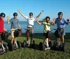 A group of five people wearing helmets are smiling and posing on Segways by the seaside