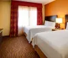 The image features a neatly arranged hotel room with a large bed a work desk with a chair a sitting area and warm-toned decor