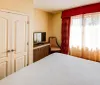 The image features a neatly arranged hotel room with a large bed a work desk with a chair a sitting area and warm-toned decor