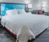 The image shows a neatly made king-size bed in a modern hotel room with contemporary decor and artwork