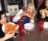 Three people are joyfully eating large slices of pizza at an outdoor table