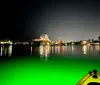 A group of people is kayaking at night with a strong green light illuminating the water and vegetation creating an eerie atmosphere