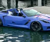 A blue sports car with pink striping is submerged in water next to a dock appearing to have accidentally driven into the water