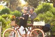 A happy couple shares an affectionate moment on a bicycle surrounded by lush greenery in a sunlit park.