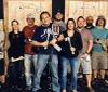 A group of cheerful people wearing matching Axe Throwing Tampa shirts pose with axes in front of a wooden target wall at an axe-throwing venue