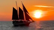 A sailboat is silhouetted against a vibrant sunset over a calm sea.