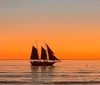 A sailboat is silhouetted against a vibrant sunset over a calm sea