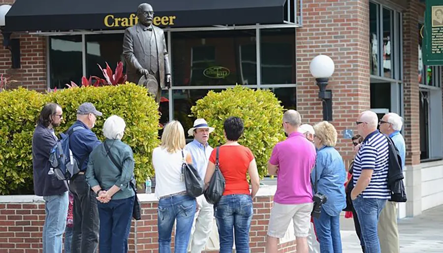 A group of people is gathered in a casual outdoor setting, engaging in conversation near a statue and a craft beer establishment.