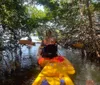 People are kayaking among the mangroves with the person in the foreground smiling for the camera