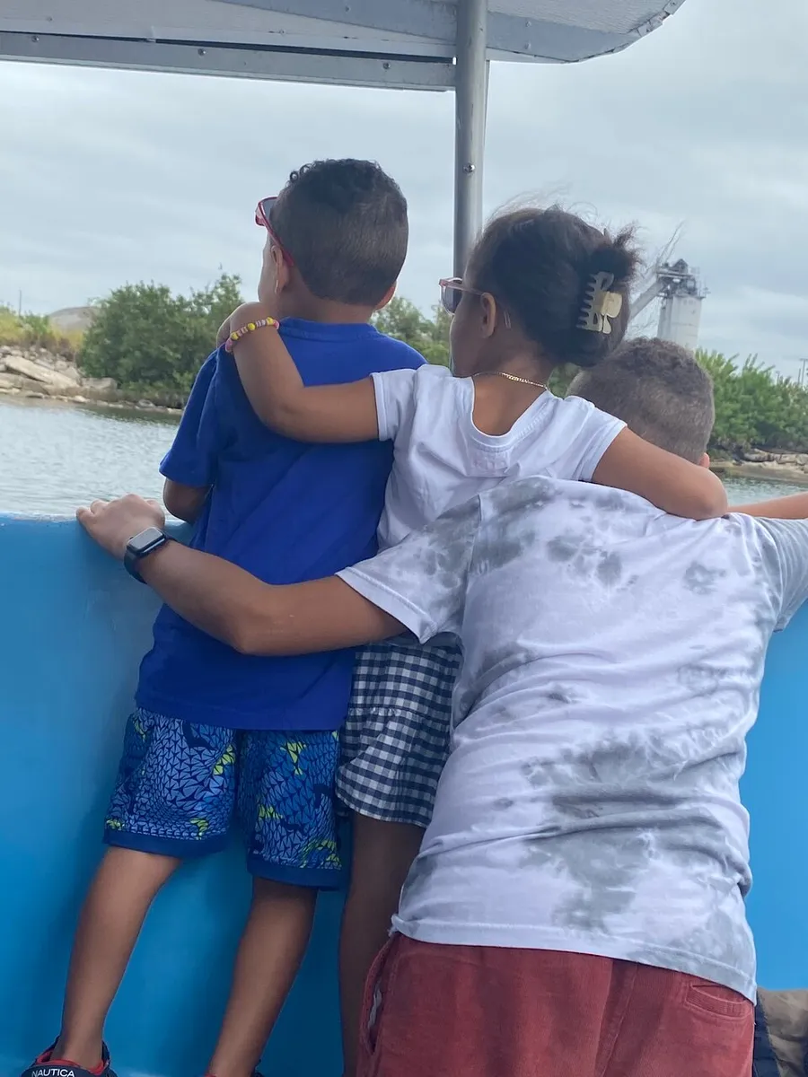 Three children are affectionately hugging each other while looking out at a view from a boat.
