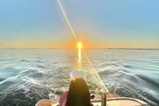 A person enjoys a serene boat ride on a calm sea under a captivating sunset.