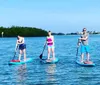 Three people are sharing a laugh while sitting on a stand-up paddleboard in calm shallow waters with others paddling nearby