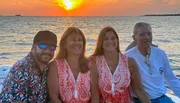 Four smiling individuals are enjoying a boat ride at sunset.