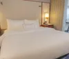 The image shows a neatly-made bed in a tidy hotel room with a desk and chair in the background