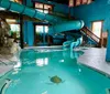 The image shows an indoor swimming pool with a spiral water slide and tropical-themed decorations