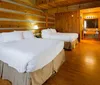 The image displays a cozy wood-paneled bedroom with two beds and an attached bathroom visible in the background