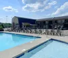An outdoor swimming pool with lounge chairs is situated in front of a motel under a clear blue sky